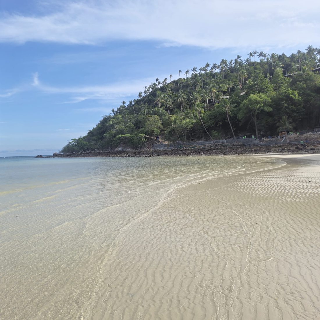 Clear, shallow water over rippled sand beside a green headland