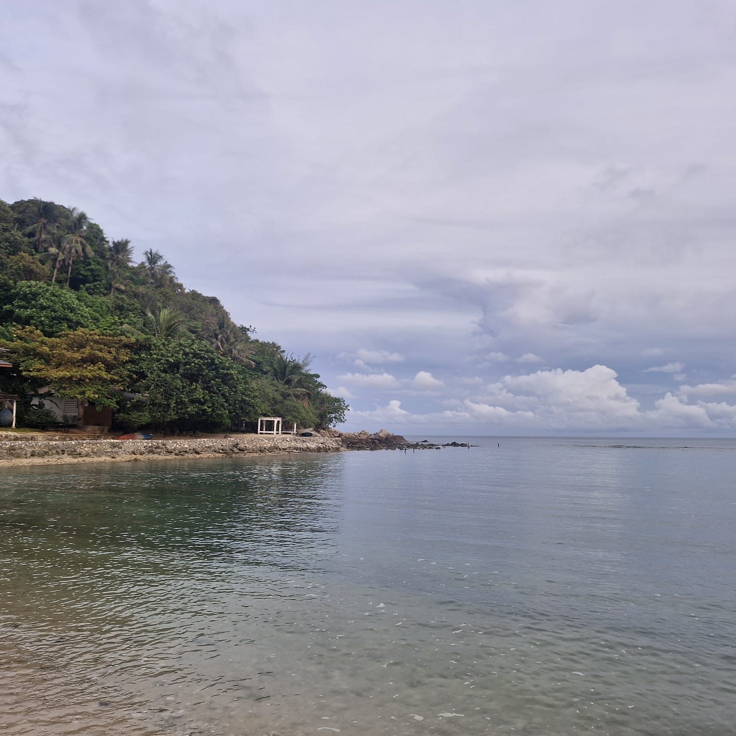 Calm, clear water beside a green point with a small white hut